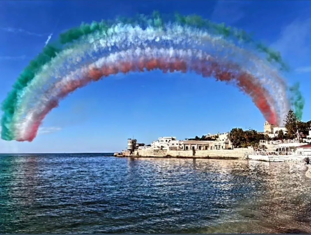 Un arco verde, bianco e rosso delle Frecce Tricolori sopra il mare e la penisola di Colonna