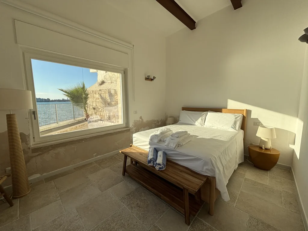 Letto matrimoniale davanti alla grande finestra sul mare con la palma