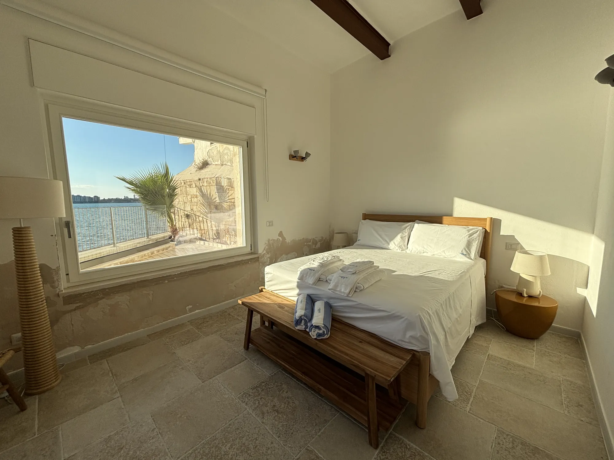 Letto matrimoniale davanti alla grande finestra sul mare con la palma