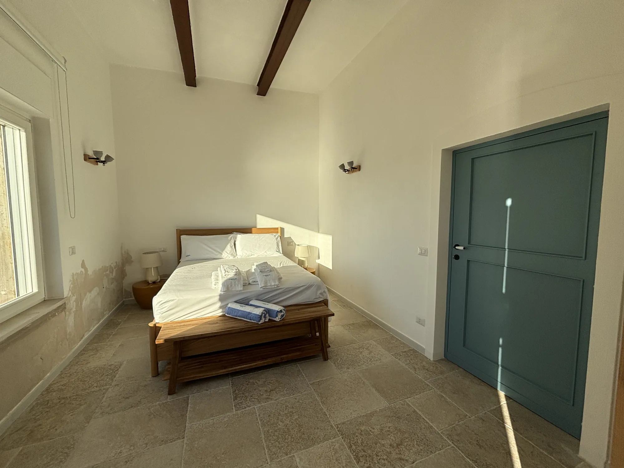 Camera con travi a vista, letto con panca e porta blu