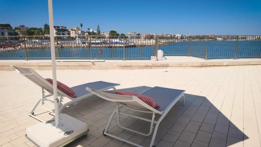 Lettini con cuscini a righe sulla terrazza, davanti al mare e al lungomare